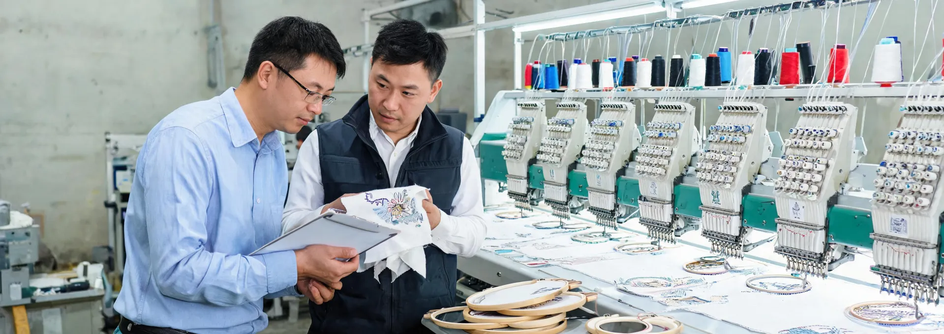 Application engineer reviewing an embroidery sample beside an industrial machine